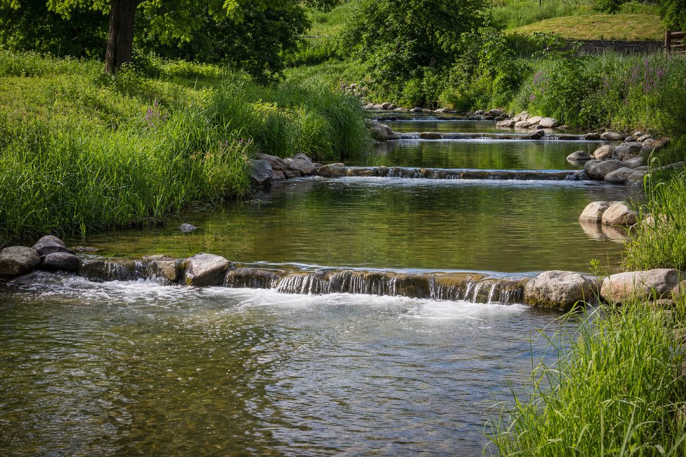 Abgestufter Fischpass mit über niedrige Wehre fließendem Wasser an einem grünen Flussufer der Regnitz